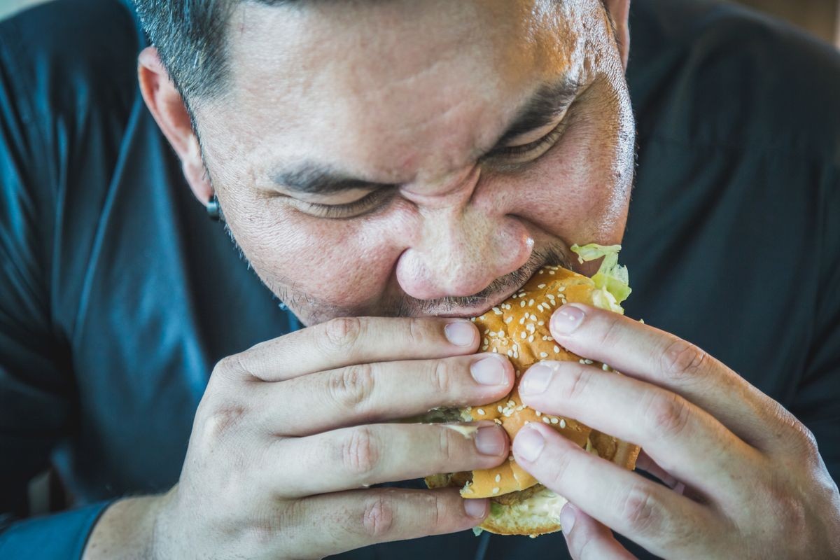 A man hands holding and eating hamburger , man enjoy to eat fast food burger , american unhealthy meal